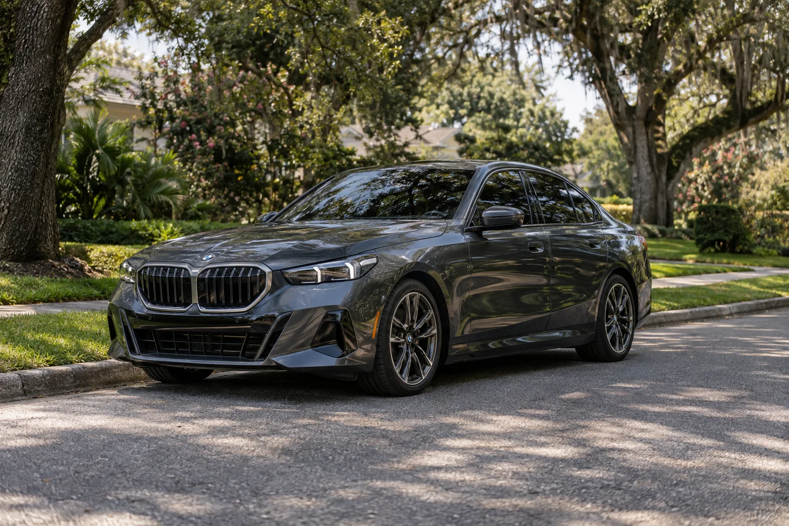 Graphite BMW 5 Series with dark tinted side and rear windows on a tree-lined Jacksonville street