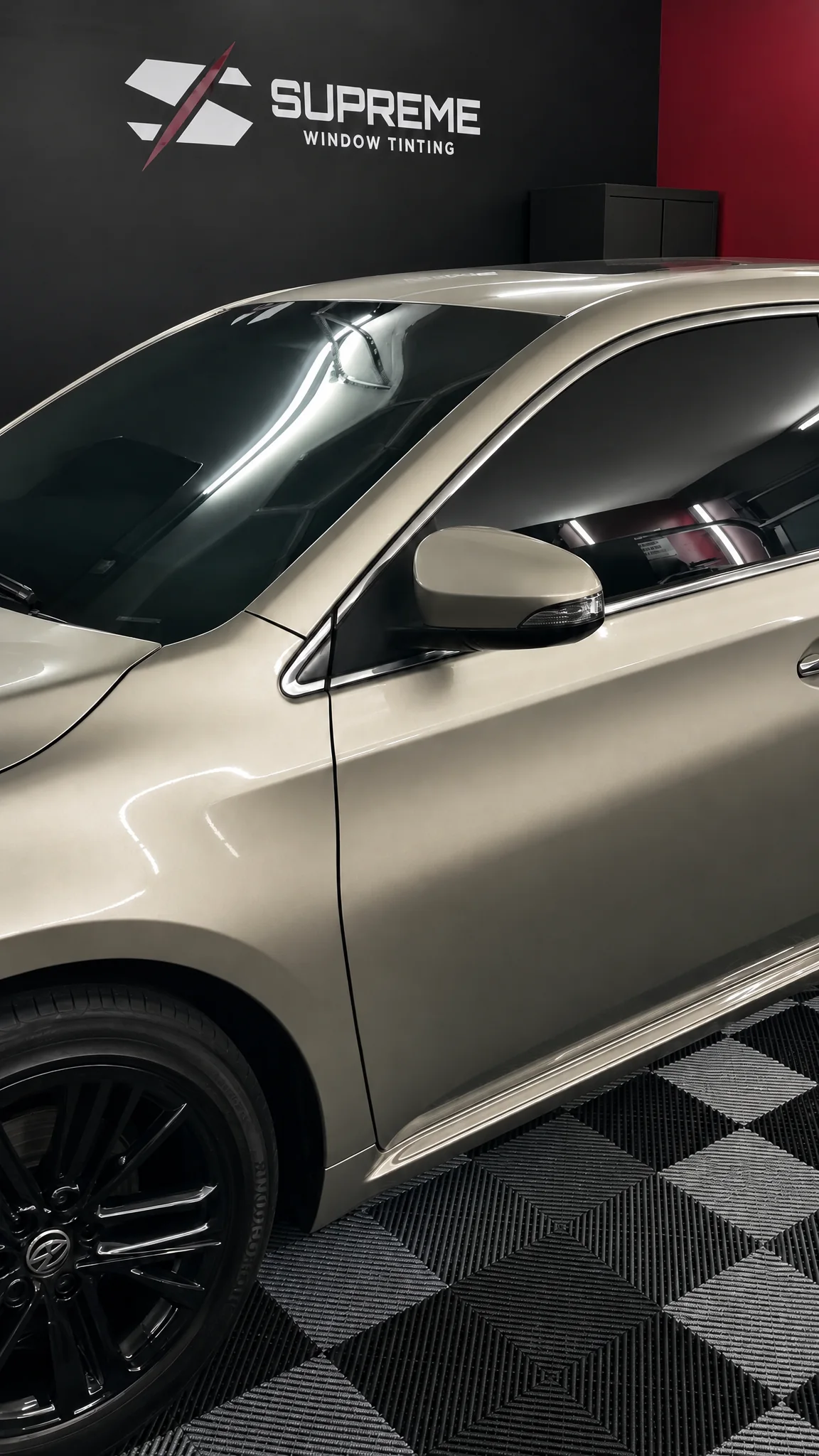 Tinted side glass on a gray sedan, indoors with the Supreme Window Tinting logo on the wall