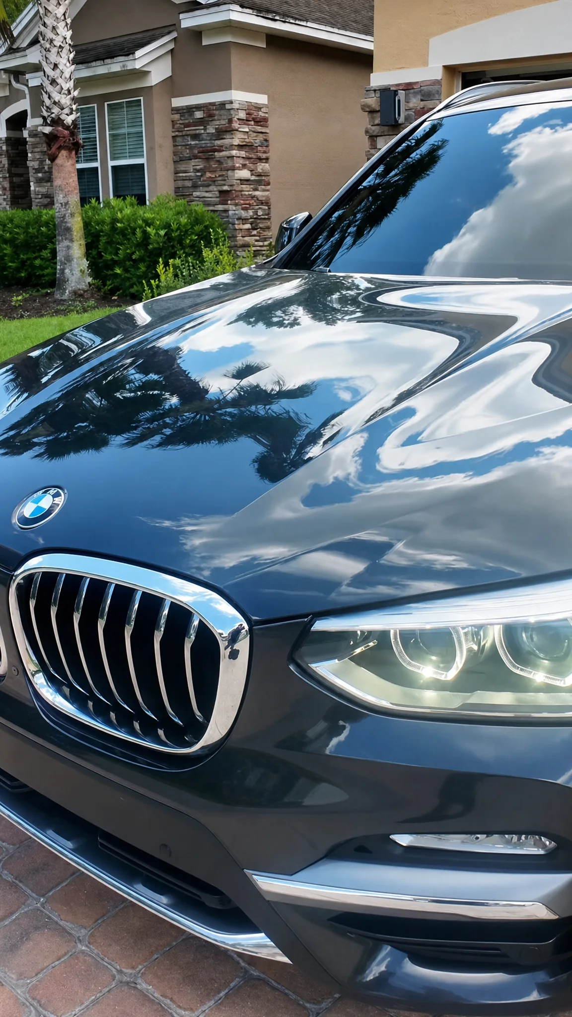 Dark BMW X3 with tinted windows, seen from the front three-quarter view with palm trees reflected